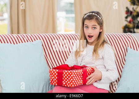 Niedliche kleine Mädchen sitzen auf der Couch mit Geschenk Stockfoto