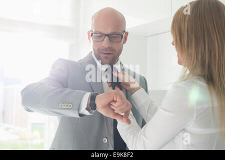 Mitte adult Check-Armbanduhr während Frau Geschäftsmann Anpassung seine Krawatte zu Hause Stockfoto