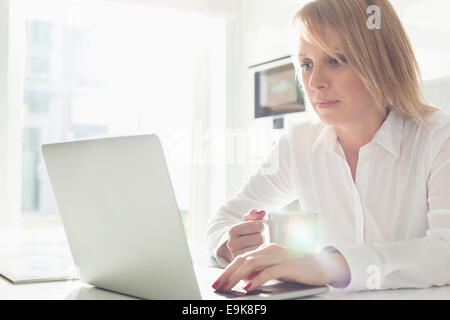Schöne Mitte adult Geschäftsfrau mit Laptop beim Kaffeetrinken zu Hause Stockfoto