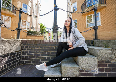 In voller Länge Portrait von junge Frau sitzt auf der Treppe gegen Gebäude