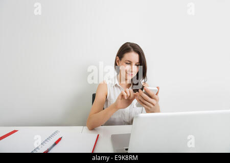 Junge Geschäftsfrau SMS über Handy am Schreibtisch im Büro Stockfoto