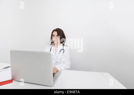 Junge Ärztin wegschauen während mit Laptop am Schreibtisch in Klinik Stockfoto