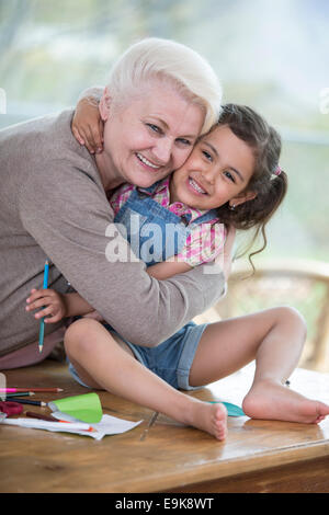 Porträt von senior Frau umarmt Enkelin auf Tisch zu Hause Stockfoto