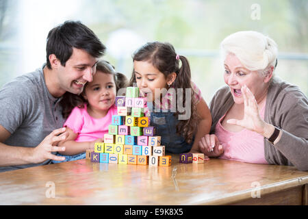 Niedliche Mädchen bläst Alphabet Blöcke während Familie sah es im Haus Stockfoto