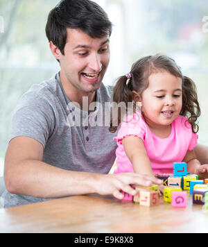 Glücklicher Vater und Tochter spielen mit Bausteinen am Tisch im Haus Stockfoto