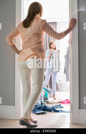 Full-length Rückansicht der Mutter beobachtete Töchter versuchen auf Kleidung im Zimmer Stockfoto