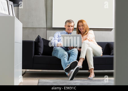 Der lächelnde paar mit Laptop auf Sofa in voller Länge Stockfoto