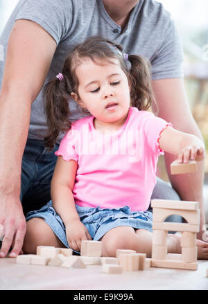 Kleine Mädchen spielen mit Holzklötzen gegen Vater im Haus Stockfoto