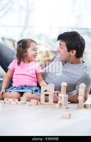 Niedliche Mädchen necken Vater während des Spielens mit Holzbauklötzen zu Hause Stockfoto