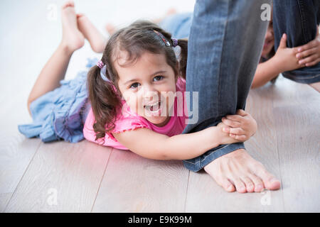 Porträt von verspielten Mädchen mit Schwester Hartholz-Fußboden des Vaters Beine festhalten Stockfoto