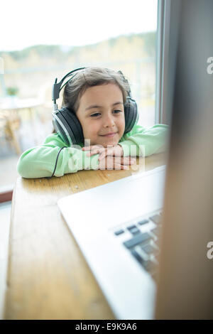 Niedliche kleine Mädchen Musik über Kopfhörer hören, während mit Laptop zu Hause Stockfoto