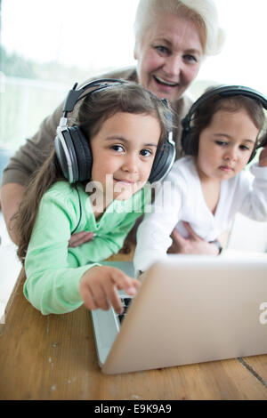 Porträt von glücklich senior Woman Enkelinnen, Musik hören, während mit laptop Stockfoto