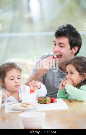 Vater und Töchter zu Hause essen Erdbeeren mit Schlagsahne Stockfoto