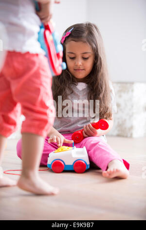 Niedliche Mädchen wählen das Spielzeug Telefon während des Spielens mit Schwester zu Hause Stockfoto