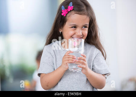 Lächelnde niedliche Mädchen hält Glas Wasser zu Hause Stockfoto