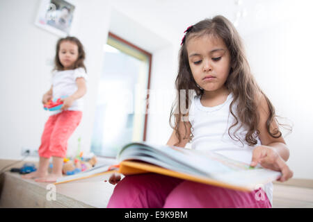 Niedliche Mädchen Buch mit Schwester spielen im Hintergrund zu Hause Stockfoto