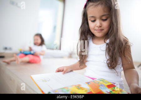 Niedliche Mädchen Buch mit Schwester im Hintergrund zu Hause Stockfoto