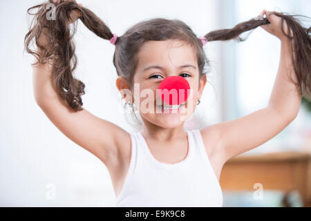 Porträt der verspielte kleine Mädchen tragen Clownsnase Zöpfen zu Hause halten Stockfoto