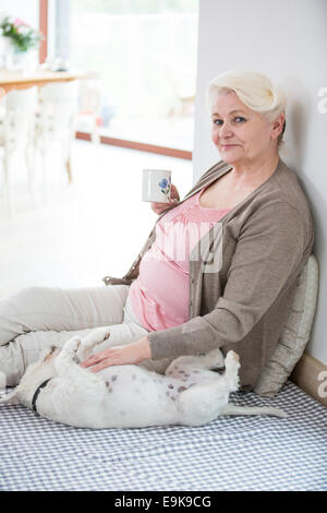 Porträt von glücklich senior Frau Kaffeetrinken während streicheln Hund zu Hause Stockfoto