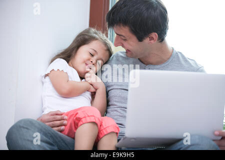 Glücklicher Vater Blick auf niedliche Tochter schlafen während mit Laptop zu Hause Stockfoto