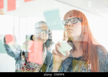 Geschäftsfrauen Haftnotizen auf Glaswand in Kreativbüro lesen Stockfoto