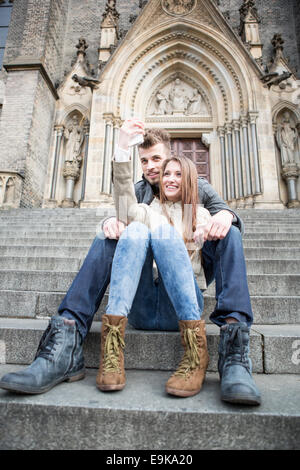 Volle Länge des jungen Paares nehmen Selfie auf Schritte im freien sitzend Stockfoto