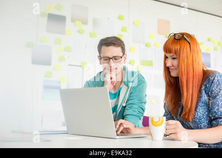 Lächelnde Geschäftsleute mit Laptop am Schreibtisch im Kreativbüro Stockfoto