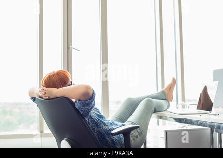 Seitenansicht der Geschäftsfrau entspannend mit Füße am Schreibtisch im Kreativbüro Stockfoto