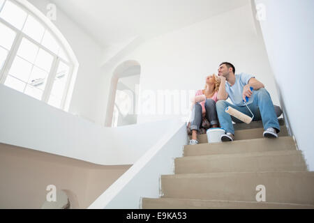 Niedrigen Winkel Ansicht des Paares mit Malerei Werkzeuge sitzen auf Schritte im neuen Haus Stockfoto