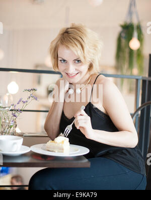 Porträt der glückliche junge Frau essen Kuchen im café Stockfoto