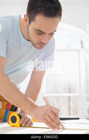 Mid-Adult Mann Kennzeichnung Tisch mit Maßband Stockfoto