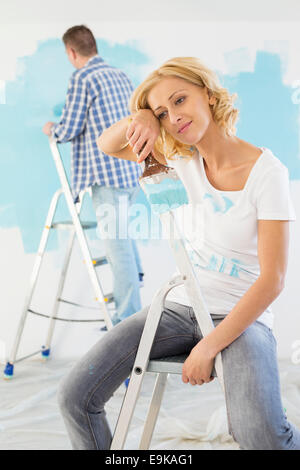 Müde Frau hält Pinsel mit Mann im Hintergrund malen Stockfoto