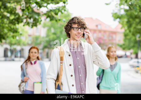 Lächelnd jungen männlichen Student mit Handy mit Freunden im Hintergrund auf Straße Stockfoto