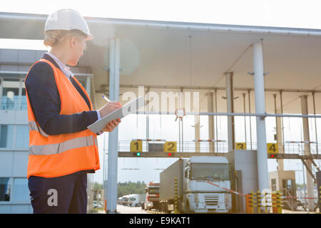 Arbeitnehmerin während der Suche bei Eingabe im Frachthafen von Trucks in Zwischenablage schreiben Stockfoto