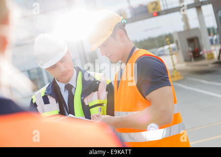 Männliche Arbeiter über Zwischenablage im Frachthafen diskutieren Stockfoto