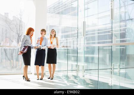Glücklich Unternehmerinnen stehen gegen die Glaswand im Büro Stockfoto