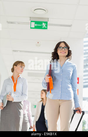 Glücklich Geschäftsfrau ziehen Gepäck während des Gehens mit Team am Flughafen Stockfoto