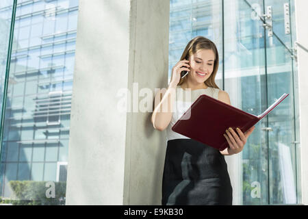 Glücklich Geschäftsfrau mit Handy beim Lesen von Datei im Büro Stockfoto