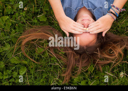 Hübsches Mädchen auf dem Rasen liegen schließt seine Augen mit den Händen. Stockfoto