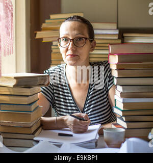 Schwere Frau in ein Notizbuch in einem Raum mit vielen Büchern zu schreiben. Vorbereitung auf Prüfungen. Stockfoto