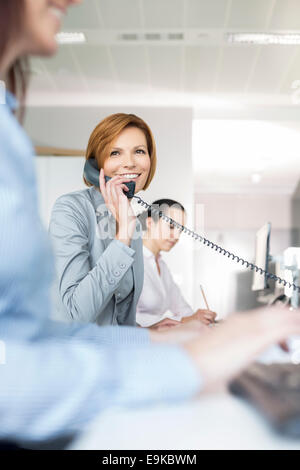 Lächelnde junge Geschäftsfrau mit Festnetz-Telefon im Büro Stockfoto