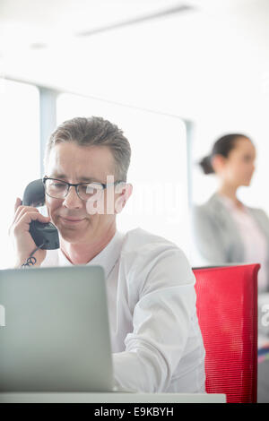 Geschäftsmann mit Kollegen im Hintergrund im Büro am Telefon sprechen Stockfoto