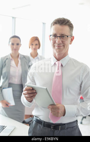 Porträt von glücklich Geschäftsmann hält digitale Tablet mit weiblichen Kollegen im Hintergrund im Büro Stockfoto