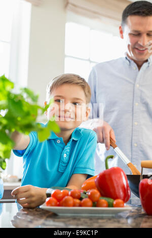 Lächelnde junge berühren Zimmerpflanze mit Vater, Zubereitung von Speisen in der Küche Stockfoto