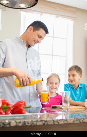Vater mit Orangensaft für Kinder in Küche Stockfoto