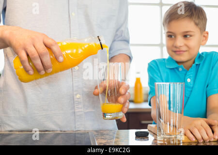 Mittelteil des Vaters servieren Orangensaft für Sohn in Küche Stockfoto