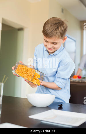 Lächelnde junge strömenden Cornflakes in Schüssel zu Hause Stockfoto