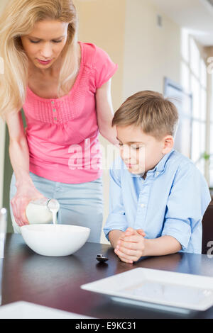 Mutter gießt Milch für Sohn am Tisch Stockfoto