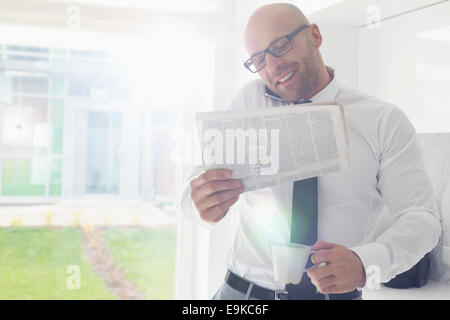 Mitte adult Geschäftsmann auf Abruf halten Sie Zeitung und Kaffeetasse zu Hause Stockfoto