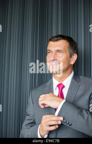 Reife Geschäftsmann knöpfte Hülse gegen Wand Stockfoto